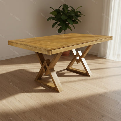 Wooden dining table with X-shaped legs in a room with a plant and window.